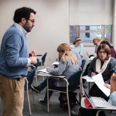 A man standing in front of a classroom full of students, giving a lecture.